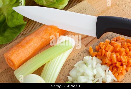 Coltello in ceramica con il soffritto sul tagliere di legno Foto Stock