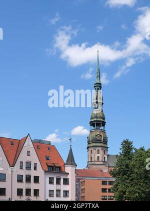 Il famoso campanile con il suo orologio della cattedrale gotica San Pietro a riga Lettonia, casa e un albero sono in primo piano Foto Stock