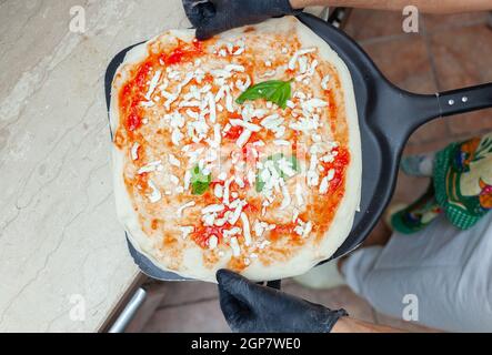 Materie pizza margherita messo sulla pala da forno per la cottura. Foto Stock
