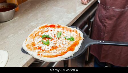 Materie pizza margherita messo sulla pala da forno per la cottura. Foto Stock
