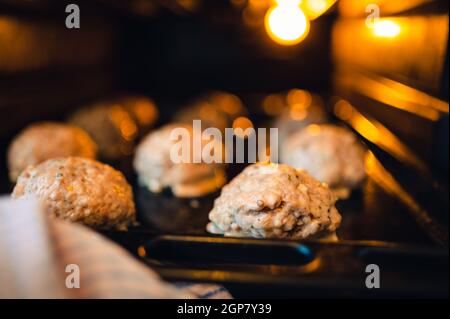 Vista nel forno sulla teglia da forno per le polpette. Poca luce, luce solo dal forno. Profondità di campo poco profonda, sfondo sfocato. Foto Stock