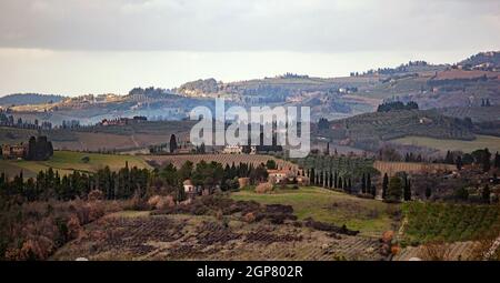 Il paesaggio toscano e strada di campagna con cipressi, alberi e palazzi antichi. Regione Toscana in Italia. Foto Stock