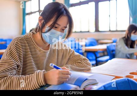 Studenti adolescenti che indossano maschere di protezione e studiano in classe Foto Stock