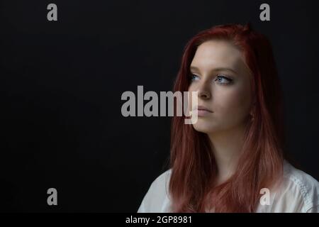 Basso ritratto chiave di bella giovane donna rossa guardando il lato. Orizzontalmente. Foto Stock