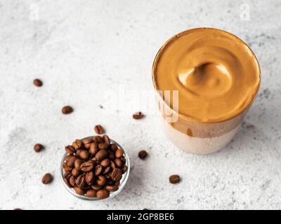 Bevanda coreana alla moda - caffè dalgona. Vaso in vetro con bevanda fredda o calda - caffè istantaneo montato con latte su fondo grigio in cemento con spazio per la copia Foto Stock