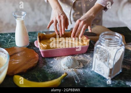 Impasto di torta cruda con banane dimezzate in ceramica a forma rettangolare. Torta alla banana Foto Stock