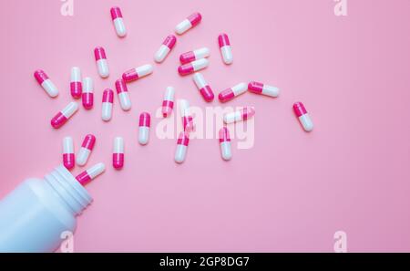 Capsule rosa-bianche la pillola è fuoriuscita dal contenitore del flacone di plastica su sfondo rosa. Resistenza agli antibiotici. Capsule antimicrobiche. Pharm Foto Stock