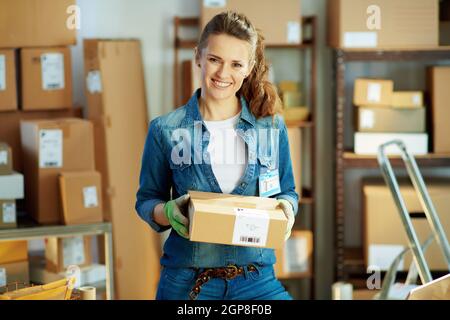 Attività di consegna. Ritratto di donna felice moderna in jeans con pacchi in magazzino. Foto Stock