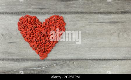 Vista superiore a forma di cuore simbolo fatta di goji (wolfberry) Bacche di colore grigio sulla scrivania di legno Foto Stock