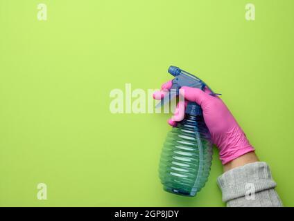 la mano femmina in guanto rosa tiene una bottiglia spray di plastica trasparente su sfondo verde, spazio per la copia Foto Stock