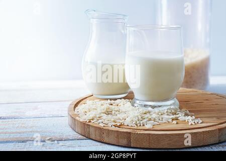 Latte di riso vegano, alternativa sana senza prodotti lattiero-caseari animali in un bicchiere da bere e una brocca su un asse da cucina di legno su sfondo chiaro, Foto Stock