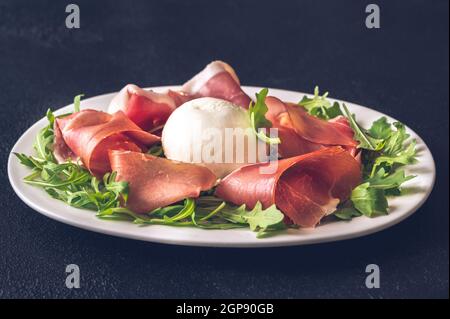 Antipasto con prosciutto, mozzarella e rucola fresca sul piatto di portata Foto Stock