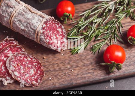 Salsiccia di prosciutto affumicata e fette tagliate con rosmarino e ciliegia pomodori su tavola di legno scuro Foto Stock