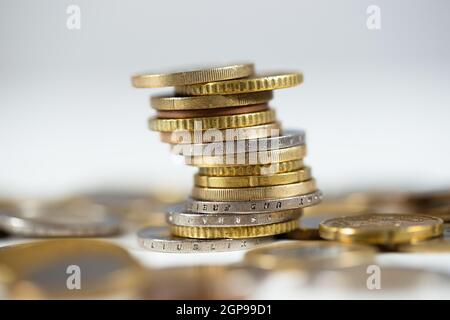 Monete metalliche in euro in piedi in un mucchio con abbondanza di altre giacenti intorno al tavolo bianco. Primo piano dettagliato del cash standing in una colonna. Concetto o Foto Stock