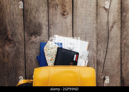 Modello da viaggio piatto con passaporti e portafoglio nero, borsa, maschera protettiva per il viso e disinfettante, blocco note e auricolari su sfondo in legno. Hig Foto Stock