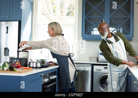 Felice senior diverse coppie in cucina indossando grembiuli, cucinare insieme Foto Stock