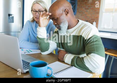 Stressato senior diverse coppie in cucina seduta al tavolo, utilizzando il computer portatile Foto Stock