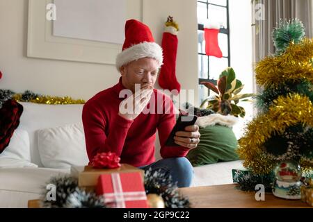 Albino african american uomo che indossa santa Hat fare videochiamata con decorazioni di natale Foto Stock