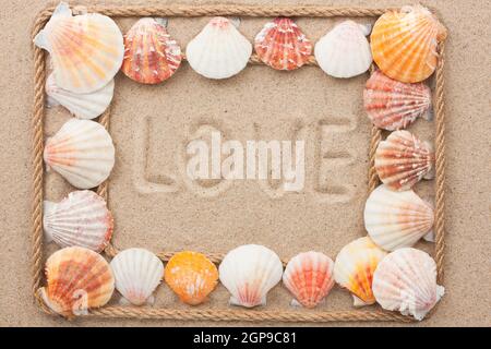 Bella cornice di corda e conchiglie sulla sabbia con testo amore, come sfondo Foto Stock