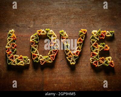 Tavolo in legno con pasta a forma di cuore che fa la parola amore. Foto Stock