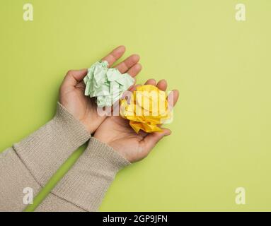 le mani femminili tengono un foglio di carta verde e giallo sbriciolato su uno sfondo verde, vista dall'alto Foto Stock
