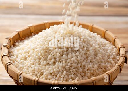 Primo piano del momento in cui il riso glutinoso viene versato in un bambù colander insieme su uno sfondo di legno Foto Stock