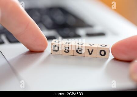 Cubi di legno con le lettere "DGSVO" per Datenschutzgrundverordnung sono giacenti su un computer portatile Foto Stock