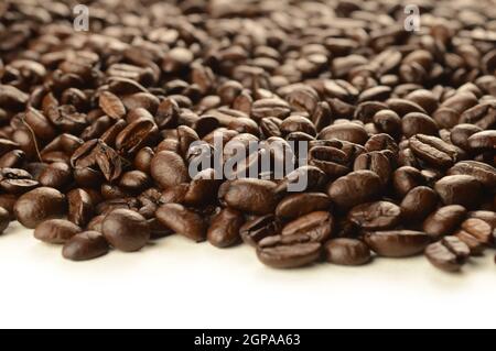 Un'abbondante quantità di chicchi di caffè appena tostati che si versano su un fondo bianco pulito. Foto Stock