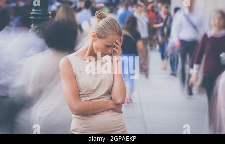 Folla di persone che camminano per la strada della città - immagine sfocata in movimento con volti irriconoscibili - giovane donna ferma, sentendosi giù, depresso Foto Stock