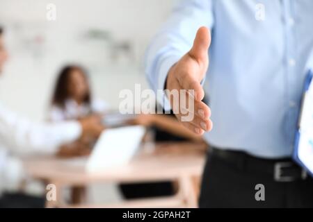 Giovane uomo che si allunga per una stretta di mano in ufficio, primo piano Foto Stock