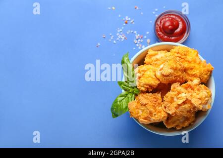 Ciotola con gustoso pollo fritto di popcorn e salsa su sfondo colorato Foto Stock