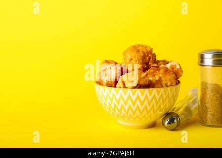 Ciotola con gustoso pollo fritto di popcorn e spezie su sfondo giallo Foto Stock