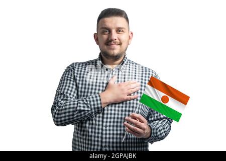 Ragazzo bianco che tiene una bandiera di Niger e tiene la mano sul suo cuore isolato su uno sfondo bianco con amore per Niger. Foto Stock