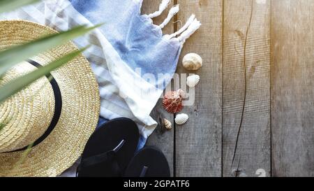 Concetto di viaggio o vacanza, fine settimana. Cappello di paglia con foglia di palma, scarpe e asciugamano, conchiglie di mare su sfondo di legno. Tempo di relax. Pho di alta qualità Foto Stock