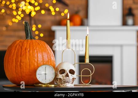 Cranio umano con sveglia, candele e zucca sul tavolo in camera Foto Stock