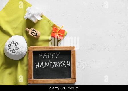 Lavagna con testo HAPPY HANUKKAH, regali, cappello ebraico e sevivon su sfondo bianco Foto Stock