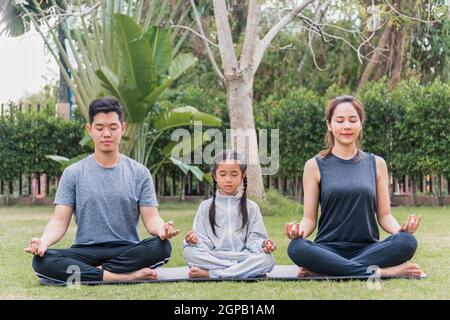 Giovane madre asiatica, padre che pratica gli esercizi di yoga con la figlia del bambino all'aperto in meditate ponga insieme nella natura un campo giardino parco, famil Foto Stock