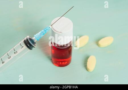 fiale per vaccino medico con liquido rosso, compressa gialla e siringa sopra la tavola verde e sfondo bianco. Vaccinazione e immunizzazione concettuale. Foto Stock