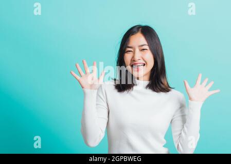 Giovane bella donna asiatica allegra sorridente trucco mostrando mani aperte, Ritratto femmina felice scioccata mostra palme, studio girato isolato su un blu Foto Stock