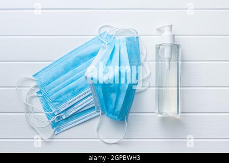 Disinfettante per le mani e maschera medica per la prevenzione del coronavirus. Gel disinfettante per le mani nel flacone della pompa sul tavolo bianco. Vista dall'alto. Foto Stock