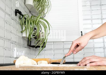 Donna che piercing l'impasto con una forchetta per cottura cieca. Le mani della donna fanno pasta per biscotti per crostate. Fare l'impasto con le mani femminili in bianco moden kité Foto Stock