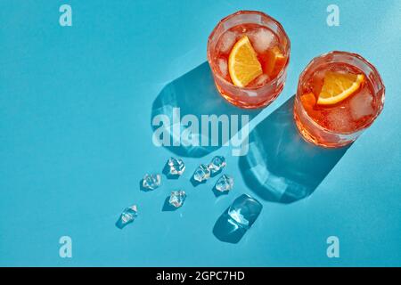 Cocktail. Succo d'arancia fresco. Due bicchieri con bevande fresche, arance affettate e ghiaccio su sfondo blu con ombra. Vista dall'alto con spazio di copia Foto Stock