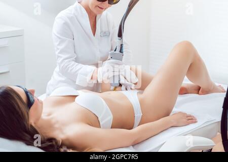 terapista che utilizza la tecnologia laser indolore per la rimozione dei capelli nella zona bikini di una cliente femminile in un moderno salone di bellezza Foto Stock