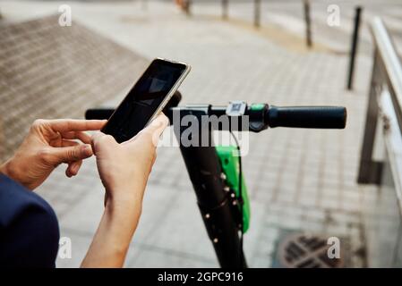Donna sblocca scooter elettrico per il noleggio utilizzando l'app per cellulare. Trasporto urbano ecologico moderno Foto Stock