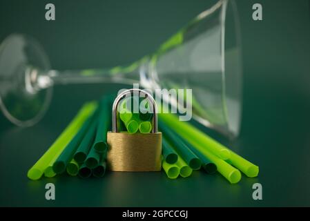 Lucchetto d'oro di fronte a cannucce di plastica per bevande su sfondo verde. Concetto di cannucce per bevande in plastica phase out Foto Stock