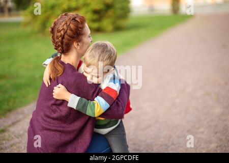 Bambino con zaino e con madre davanti ad un edificio scolastico. Concetto di maternità e mendicante della scuola primerita. Foto Stock