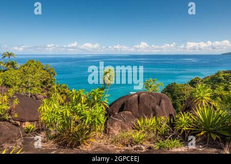 Vista da anse principali sentiero natura oltre la costa nord-ovest dell'isola di Mahe e roccia di granito in primo piano, Seicelle Foto Stock