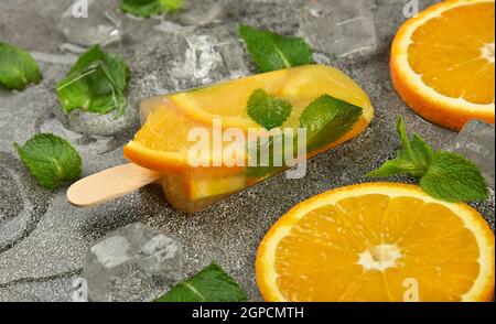 Primo piano un fungo di gelato alla frutta con fette di arancia fresca, foglie di menta verde e cubetti di ghiaccio sulla superficie grigia del tavolo, vista ad angolo alto Foto Stock