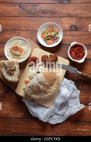 Falafel in pita pane con insalata di verdure, salsa di harissa, humus, tahini su sfondo di legno. Cucina tradizionale israeliana. Conc. Fast food medio-orientale Foto Stock