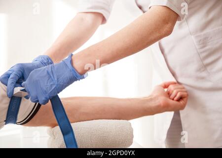 Nurse fissa il tourniquet medico sul braccio prima di prendere l'esame del sangue. Foto Stock